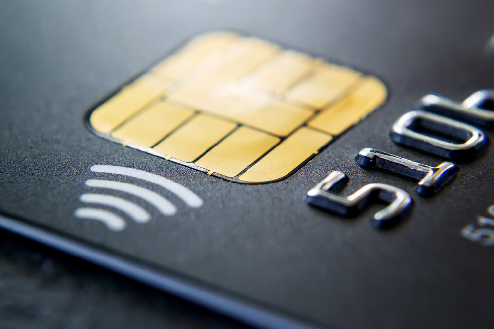 Close-up of black plastic credit card with chip and contactless pay technology. Macro photography of a bank credit card on a table.