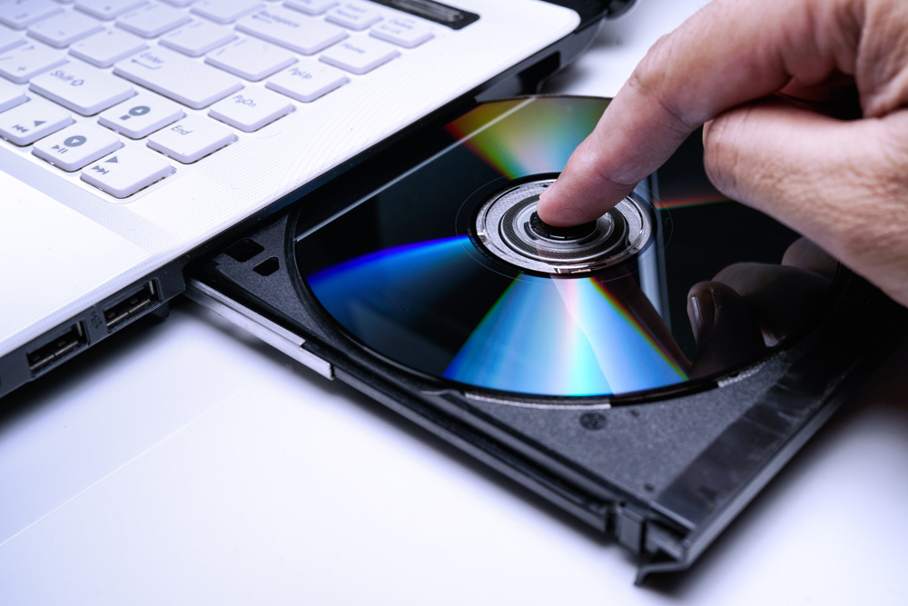 DVD Disk on the white Laptop DVD ROM Tray with a Man Hand. A Pir DVD Disk on the white Laptop DVD ROM Tray with a Man Hand. A Pir
