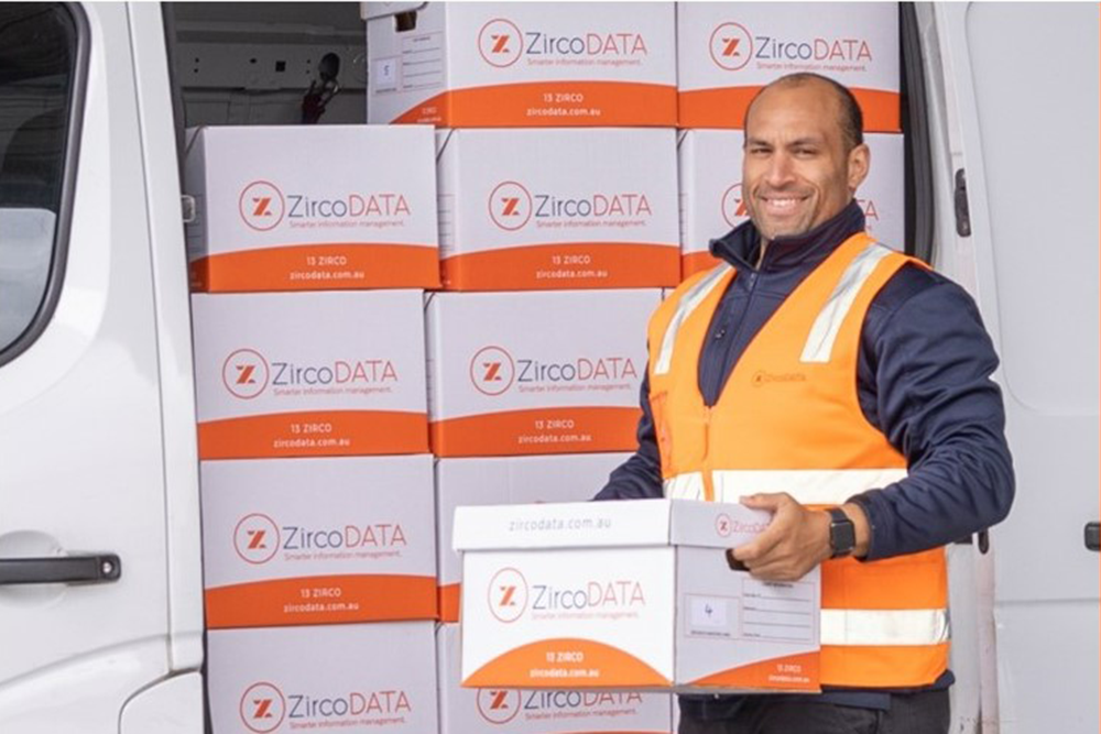 Man holding a ZercoDATA box standing in front of a van full of more boxes.